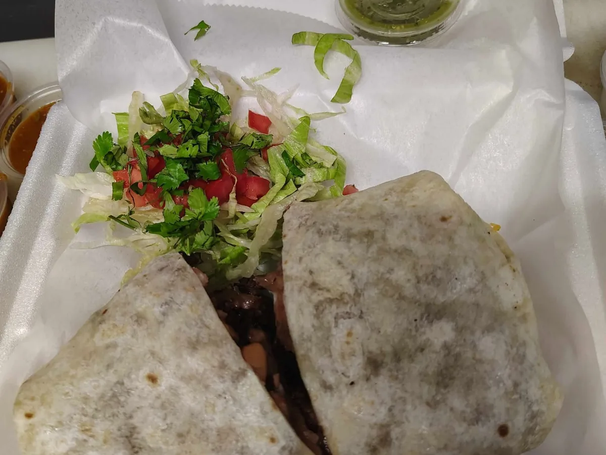 Burrito de carne asada cut in half and topped with lettuce and pico de gallo