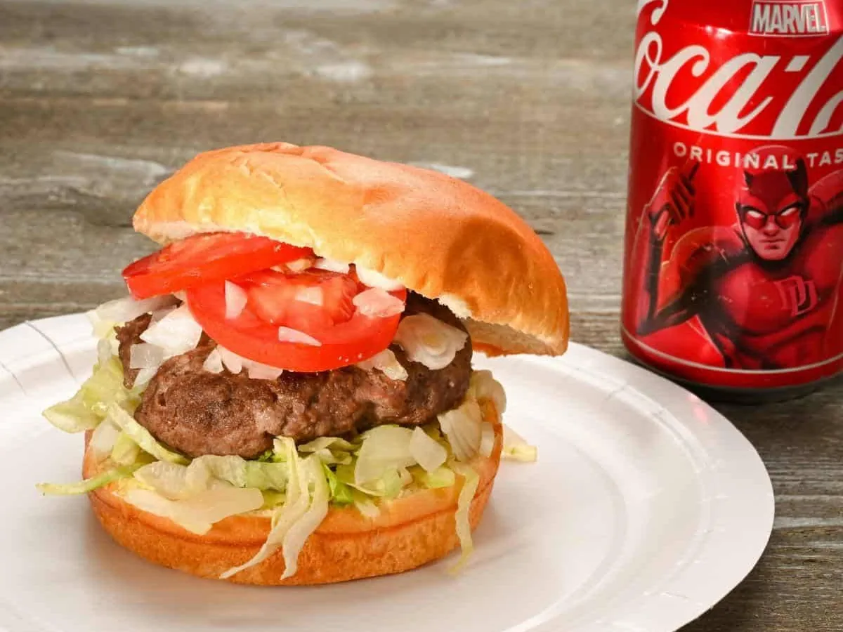 Hamburguesa with lettuce, tomato and onion served with a can of soda