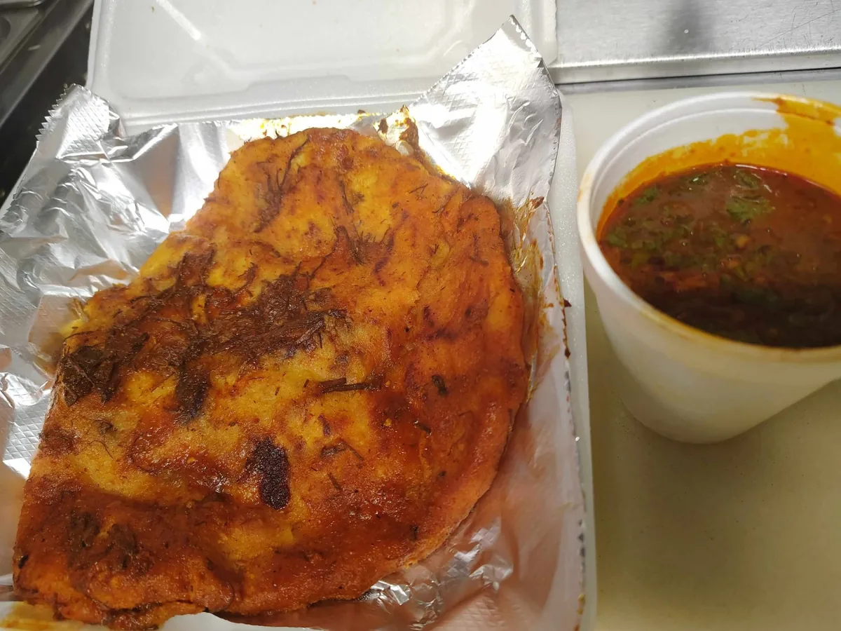 Pupusa de birria served with a cup of consomé